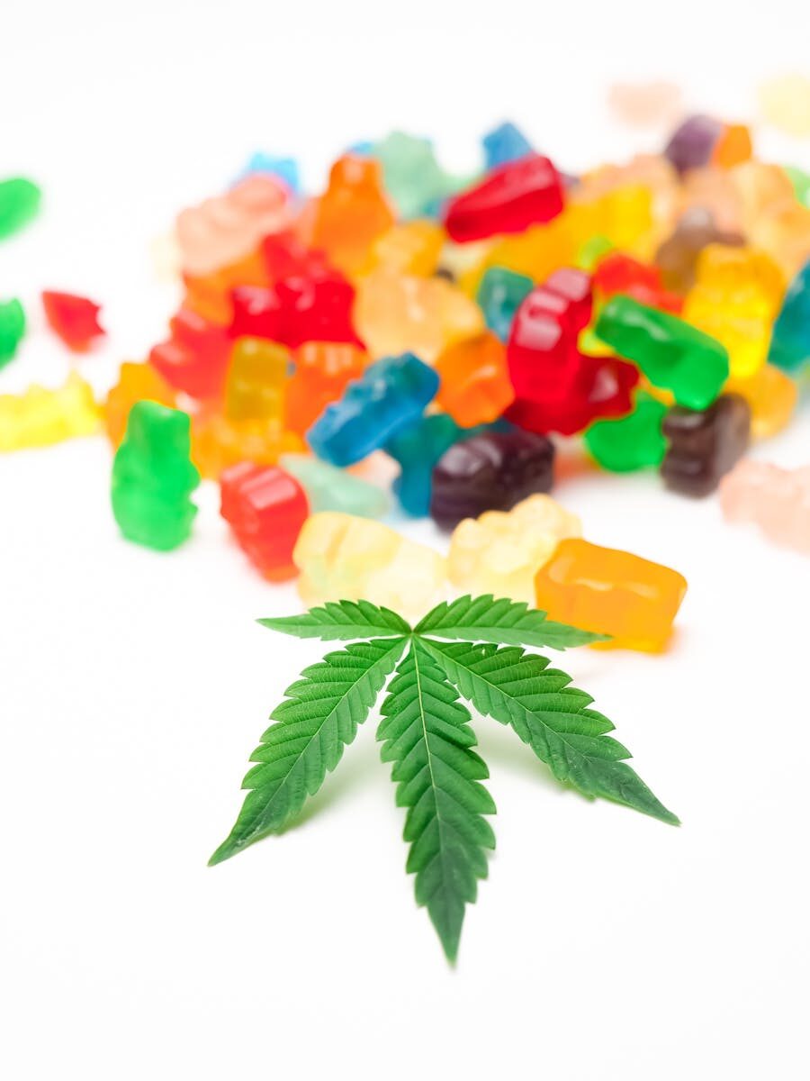 A collection of vibrant gummy bears with a single cannabis leaf focused in foreground.